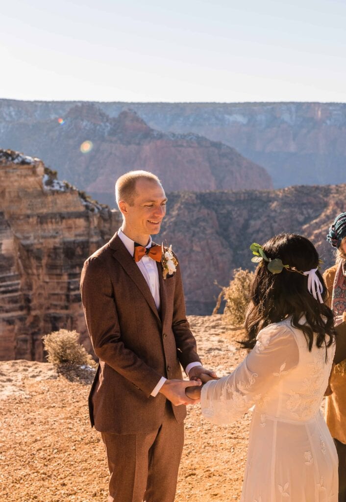 Groom smiling at bride in brown suit with red bowtie during Grand Canyon Ceremony