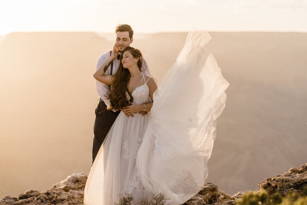 Bride and groom holding each other in front of sunset at the grand canyon south rim at lipan point lookout after their vow renewal elopement