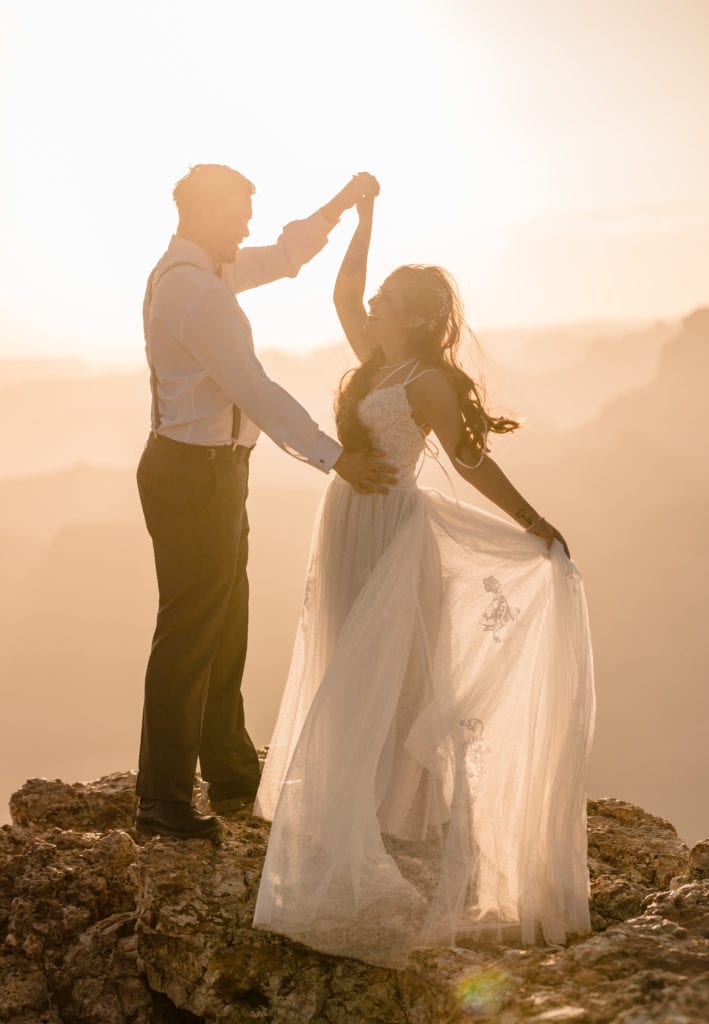 Groom spinning bride as she holds her wedding dress watching the sunset at lipan point in the Grand Canyon National Park.