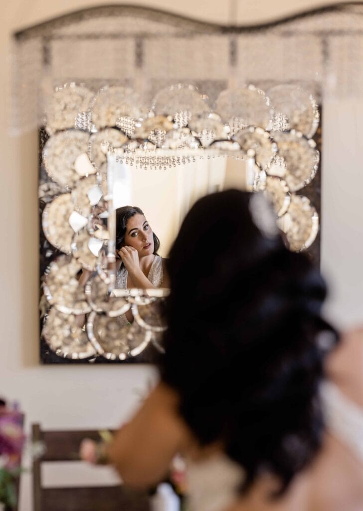 Bride looking in mirror putting earrings in .Getting ready for her Big Sur elopement.