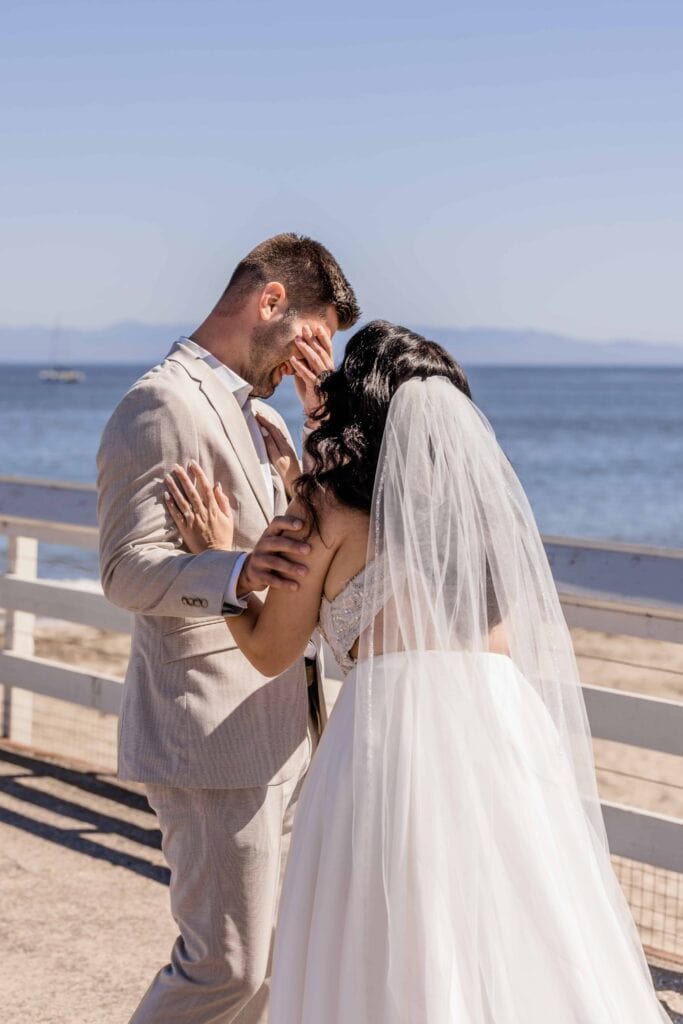 Groom covering eyes from happiness during first look on their Santa Cruz pier beach wedding.