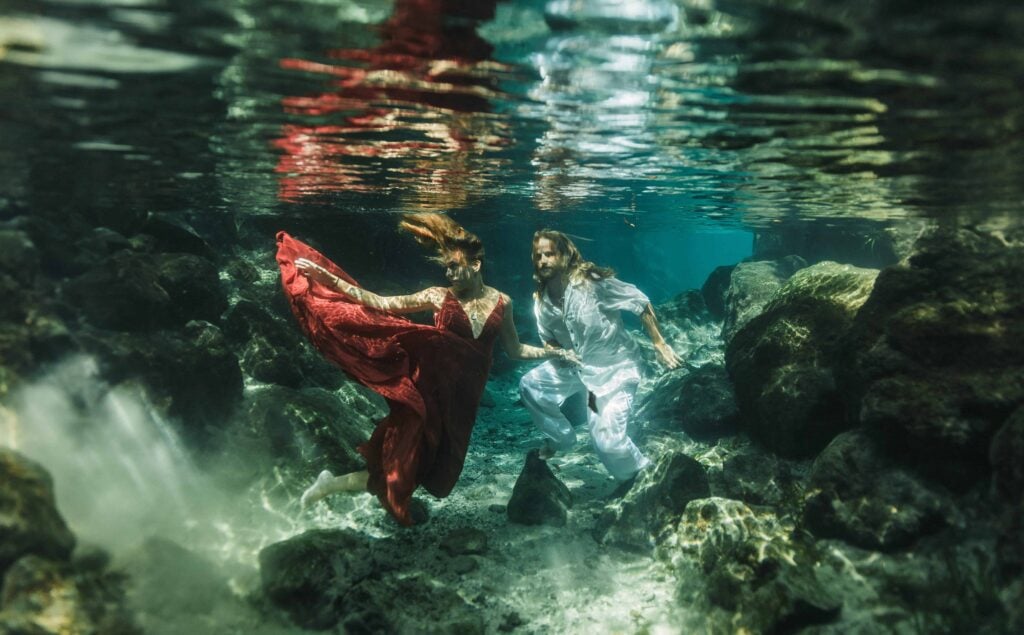 couple wearing a red dress and a white outfit underwater at the three sister springs