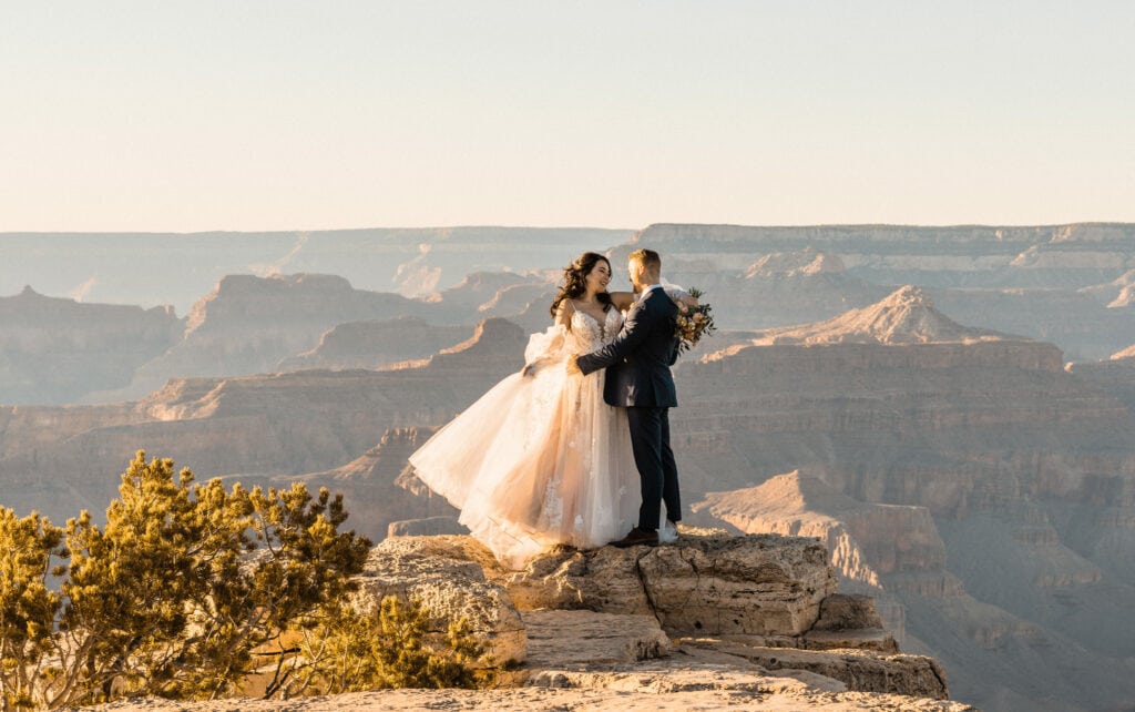 Standing in front of the grand canyon a boho bride is swaying her dress looking into the grooms eyes after their intimate wedding
