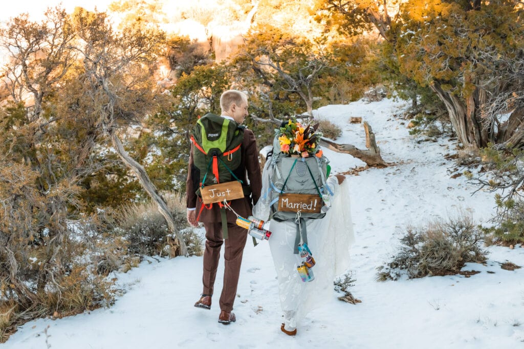 Bride and groom walking in winter snow at the grand canyon wearing just married backpacks