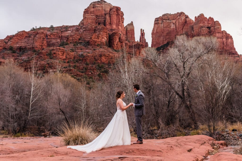 Bride and groom holding hands in front of Cathedral Rock in Crescent Moon Ranch during their elopement