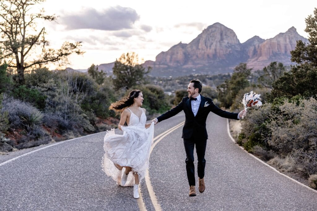 Bride and Groom running down street with red rock mountains in Sedona Arizona in the background