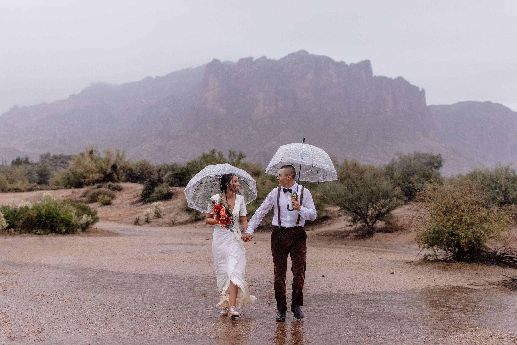 couples walks with umbrellas at rainy Superstition Mountain elopement