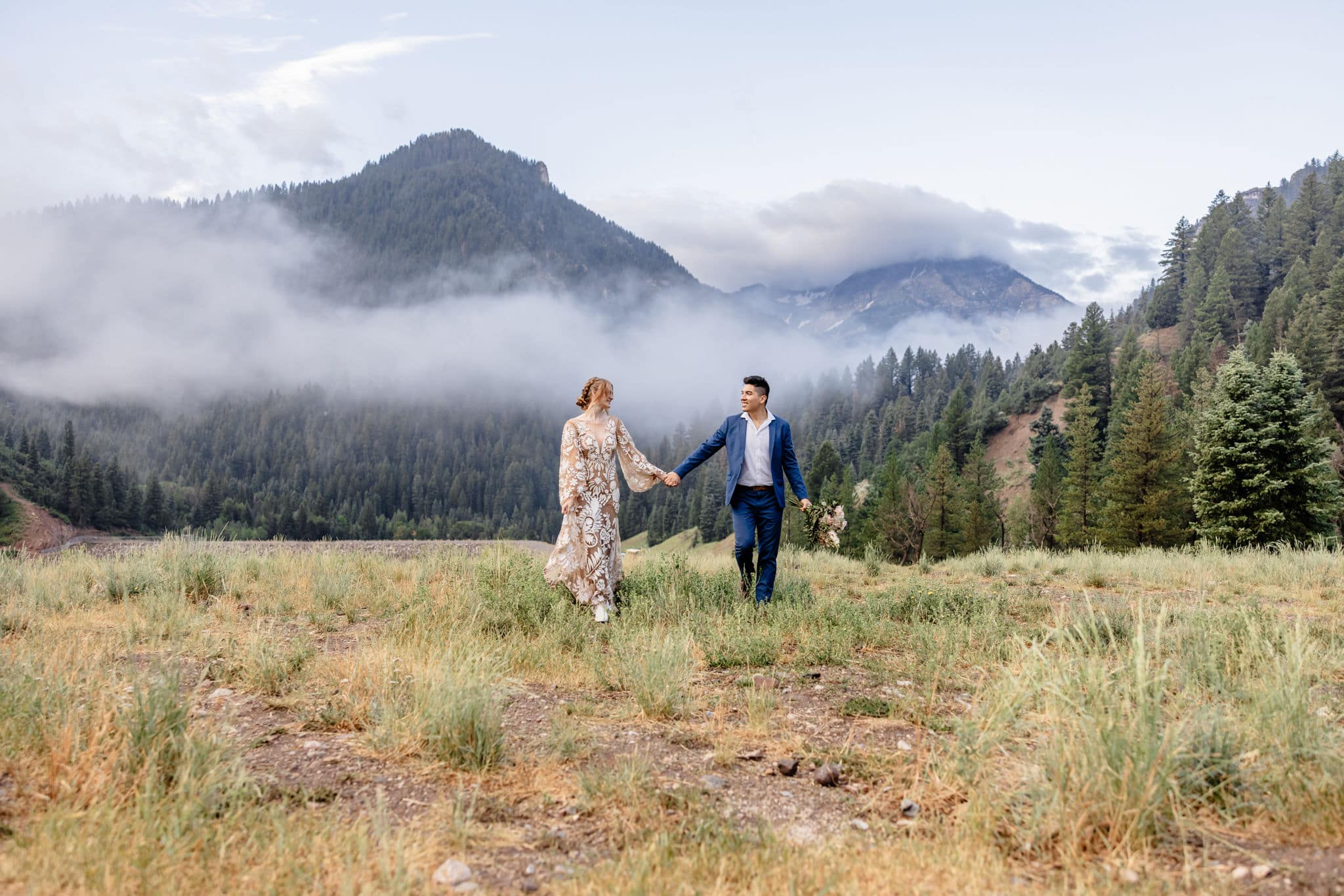 couple walks holding hands at foggy mountainside elopement