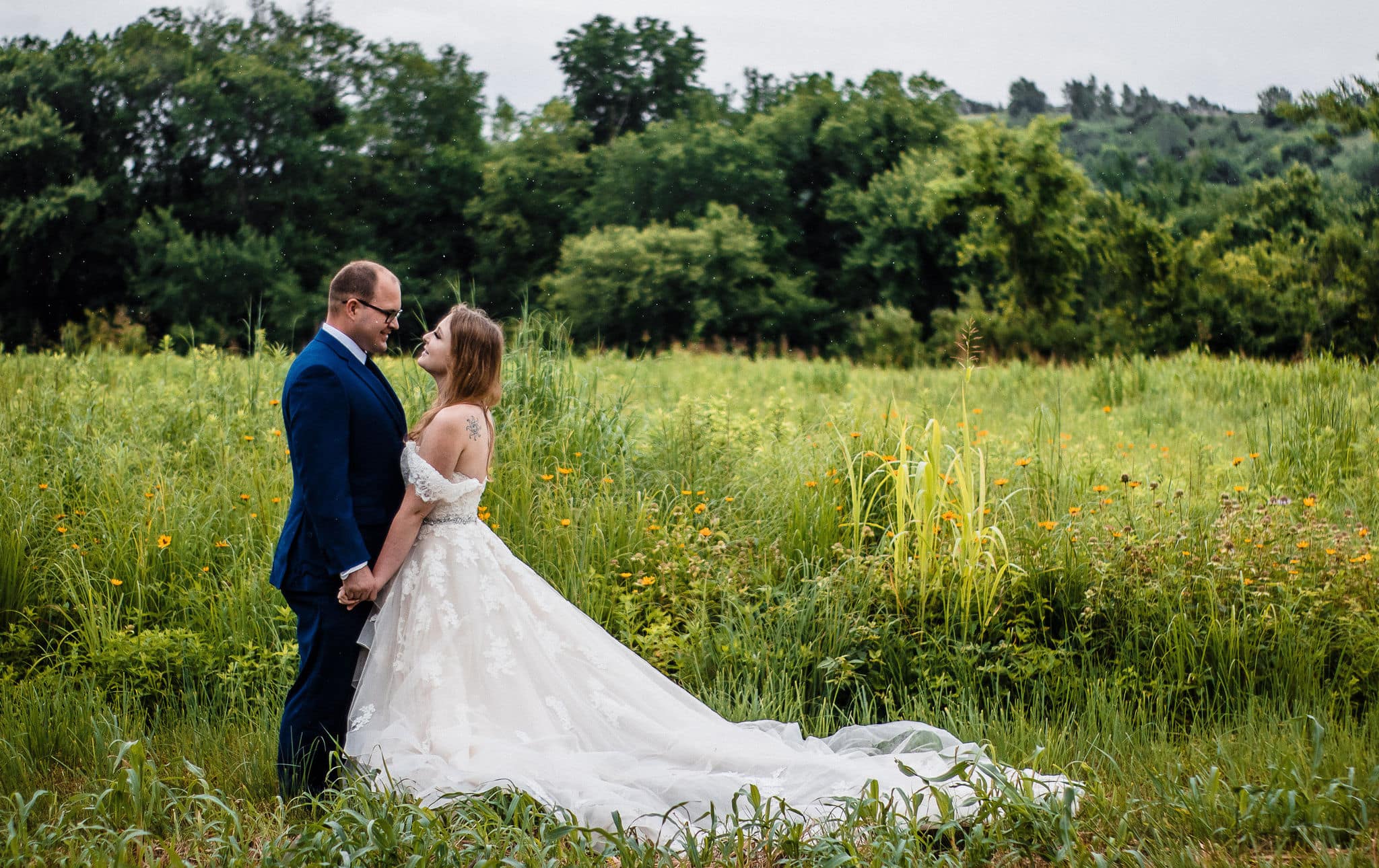 couple holds hands in green wildflower fields